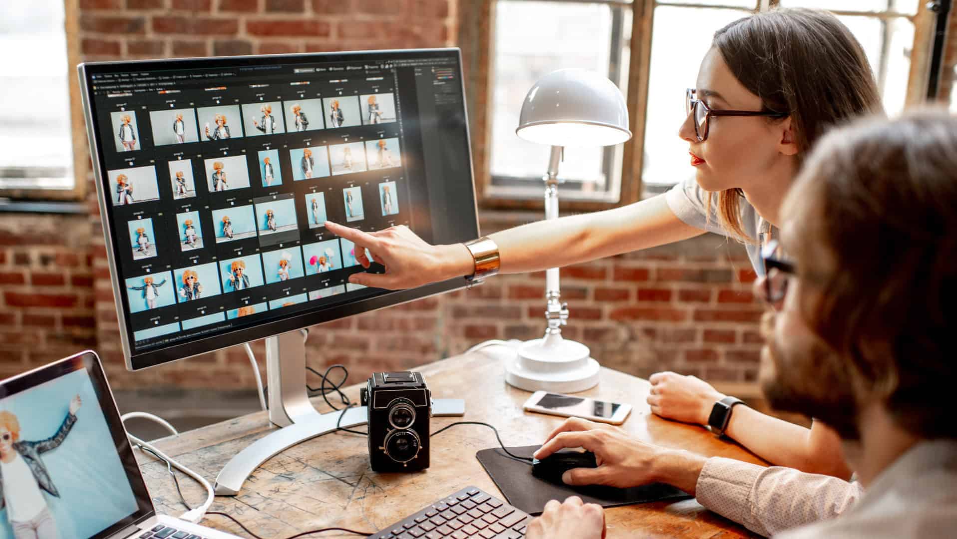 A man sitting at a desk while a woman points at a photo on the computer monitor as they work on image SEO.