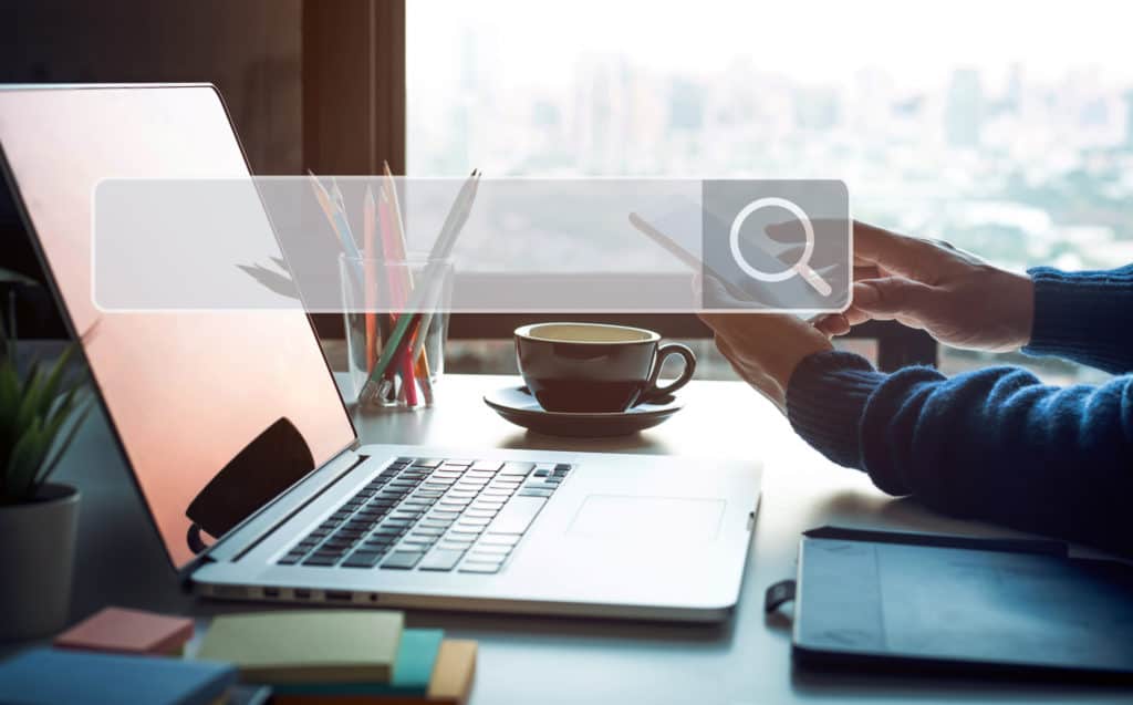 image-of-arms-resting-on-desk-with-laptop-coffee-cup-sticky-notes-and-pencils-with-search-engine-search-bar-superimposed-over-image-as-on-page-seo-concept