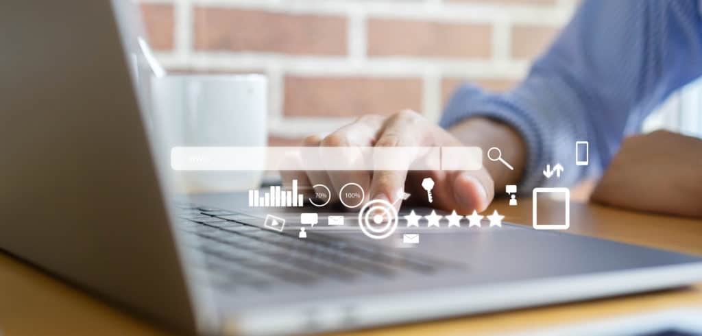 A laptop with a hand on the keyboard and an overlay of a white search bar and various seo icons