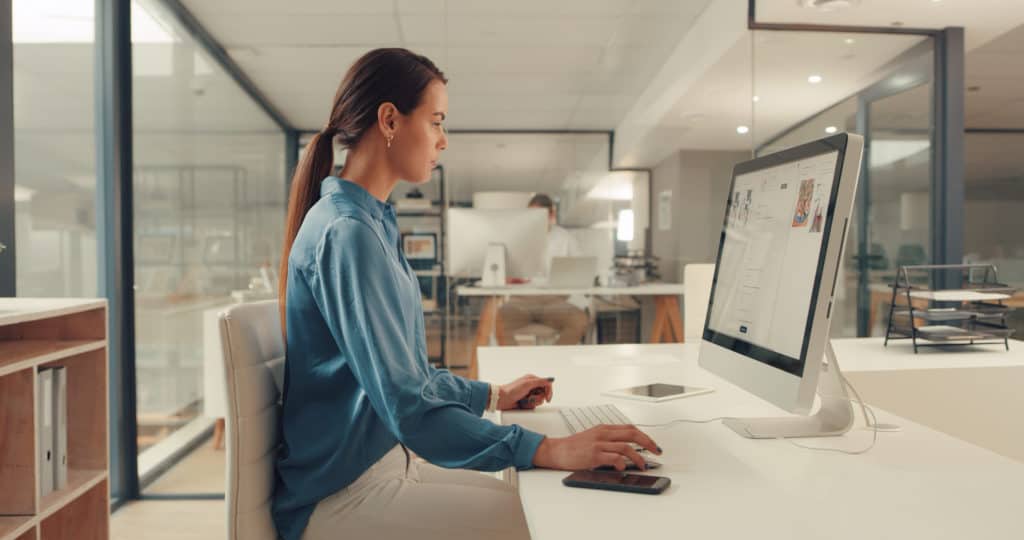 A woman in profile sitting at a desk and working on image SEO on a computer monitor with a mouse and keyboard.